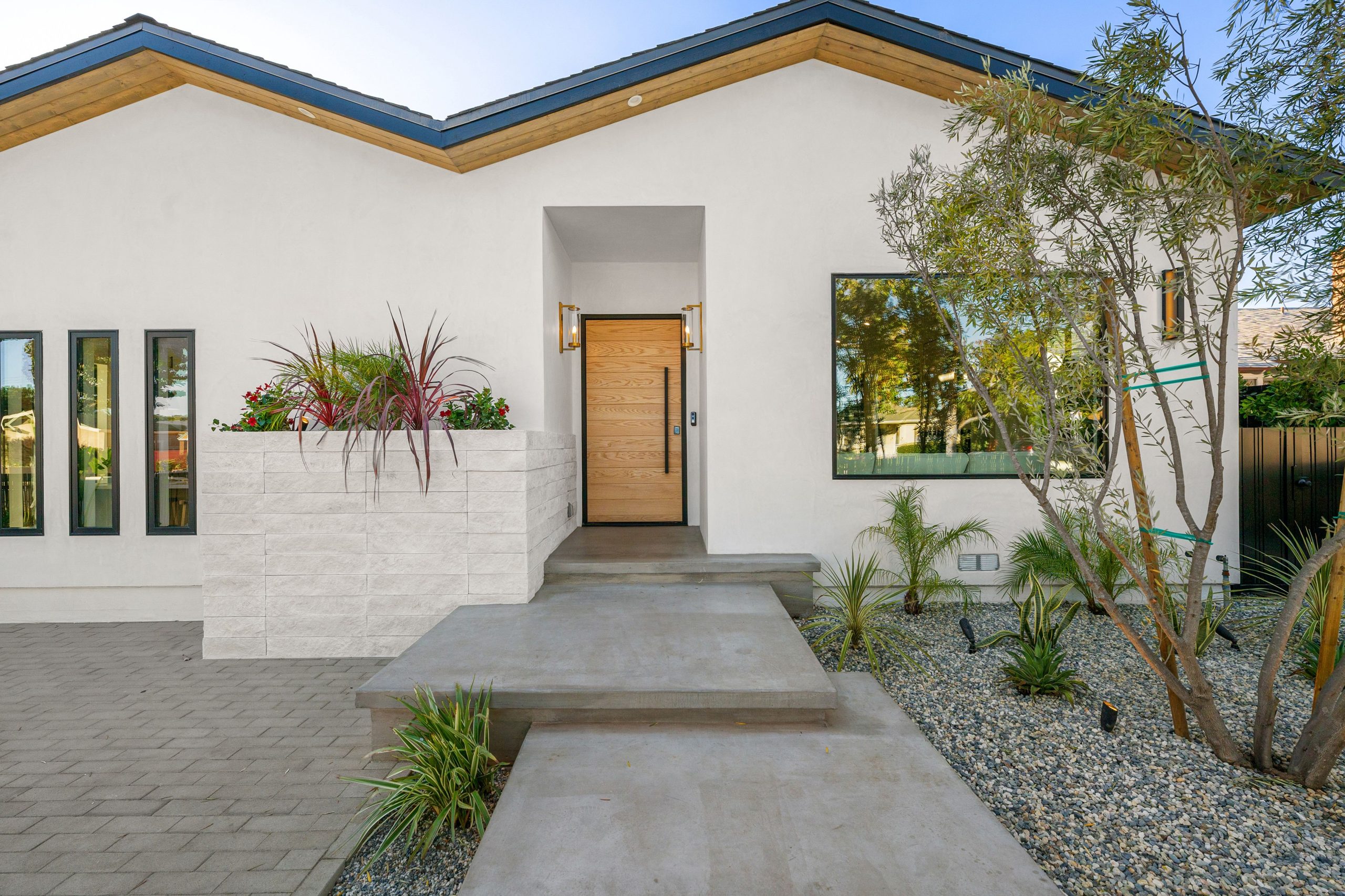 Modern home exterior with minimalist landscaping and a wooden front door under a clear sky.