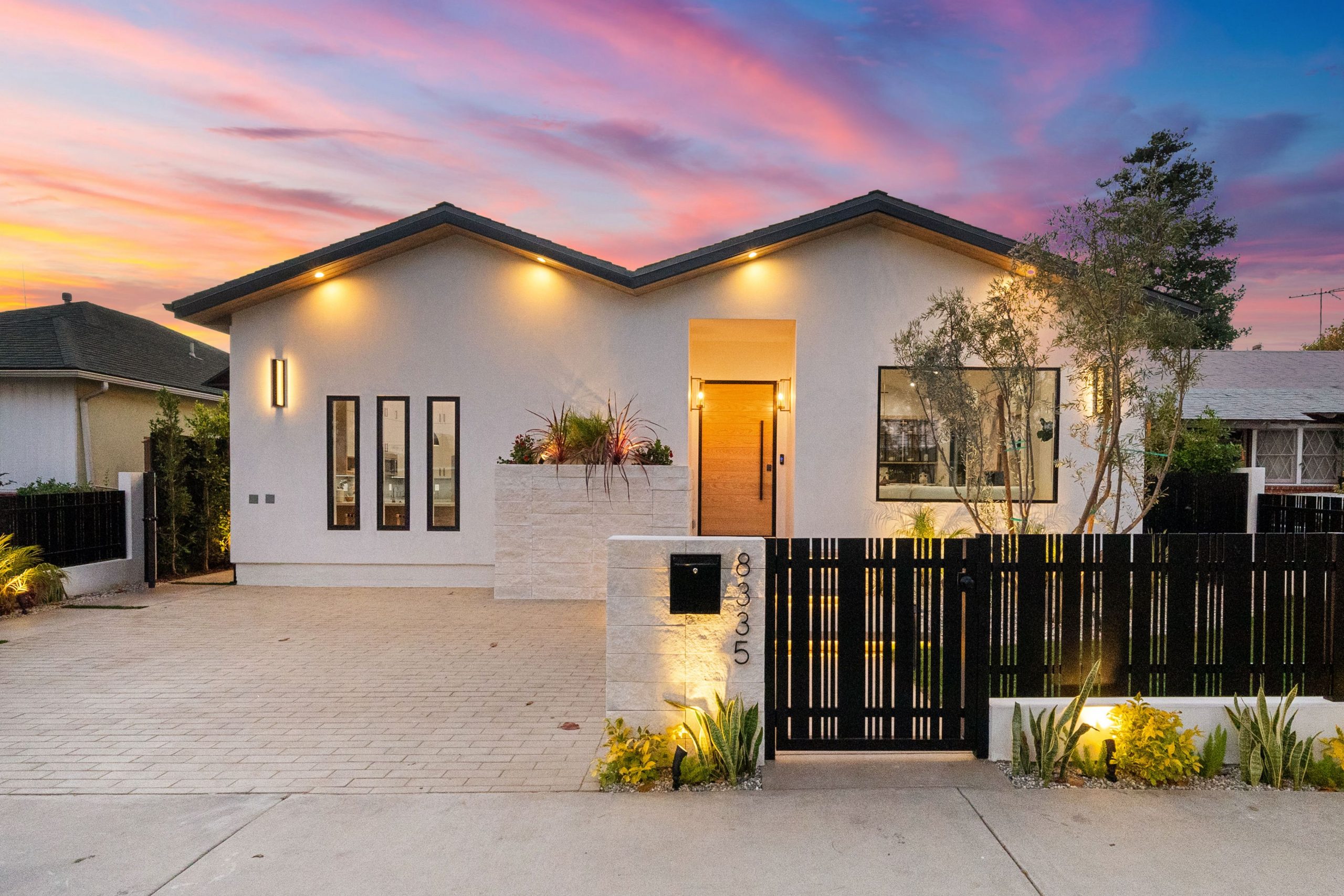 Modern house exterior with illuminated facade and vibrant sunset sky, featuring sleek design and landscaped front yard.